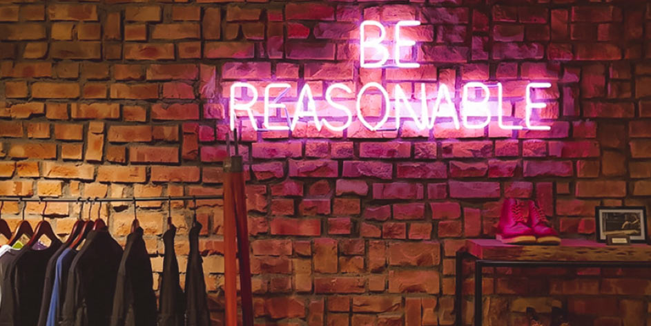 Roze Neon tekst Be reasonable bij een rek met duurzame kleding